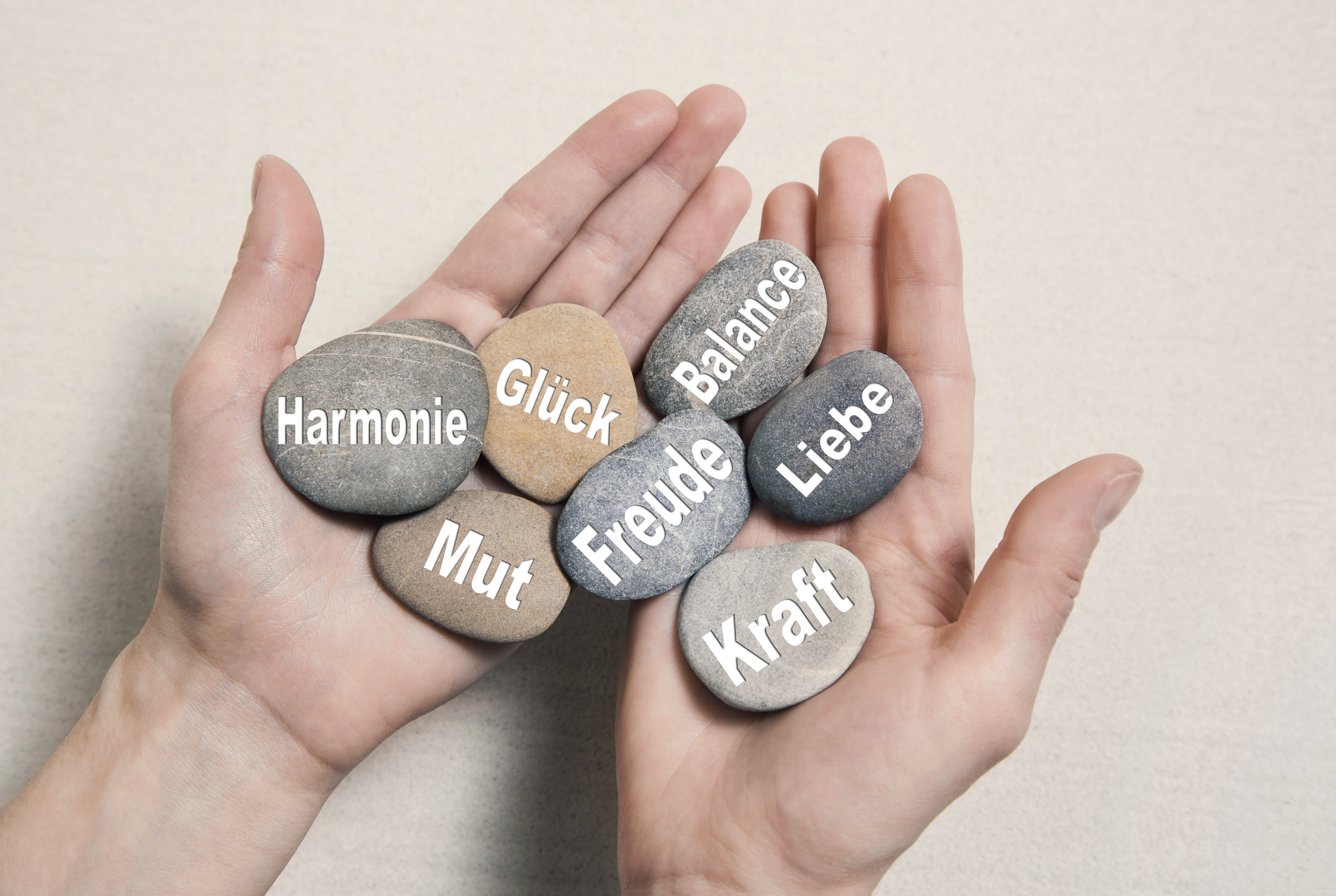 Unterstützung von Selbsthilfegruppen - Zwei Hände halten mehrere Steine mit den Worten Glück, Mut, Kraft, Freude, Harmonie, Liebe und Balance darauf